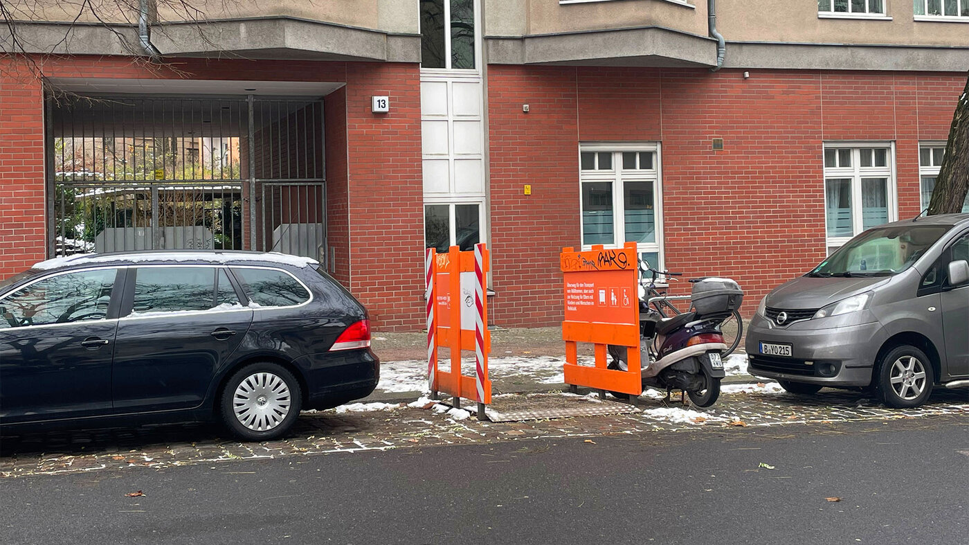 Eine Parklücke in einem Berliner Wohngebiet ist durch einen orangefarbenen Transportüberweg freigehalten.