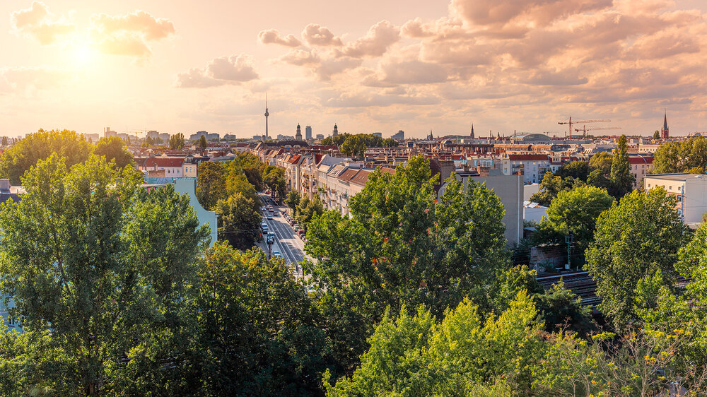 Blick über Berlin mit Wohnhäusern, Bäumen und Fernsehturm bei Sonnenuntergang