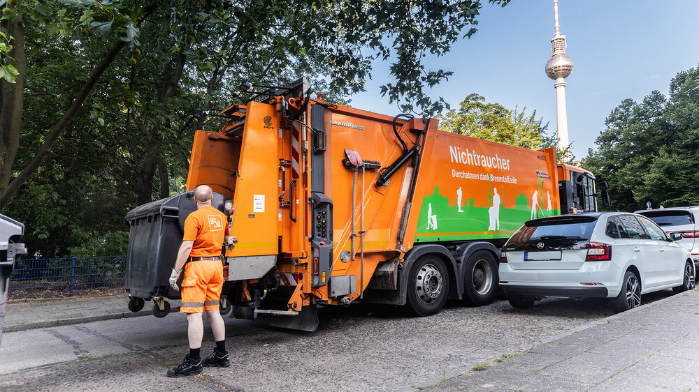 Ein BSR-Mitarbeiter steht hinter einem Abfallsammelfahrzeug, das in einer Berliner Straße im Einsatz ist