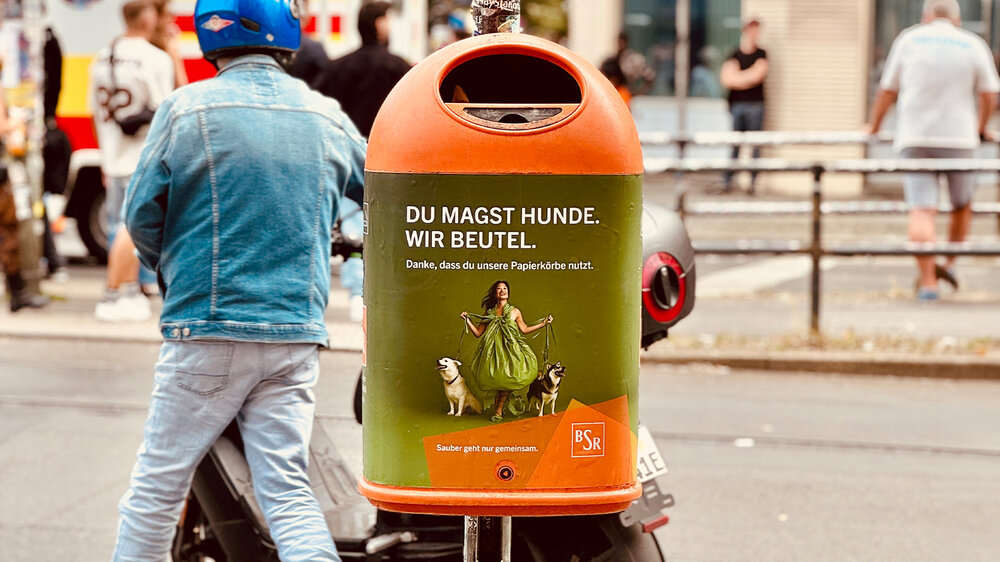 Abfallbehälter auf einer Berliner Straße mit dem Kampagnenslogan „Du magst Hunde. Wir Beutel.“
