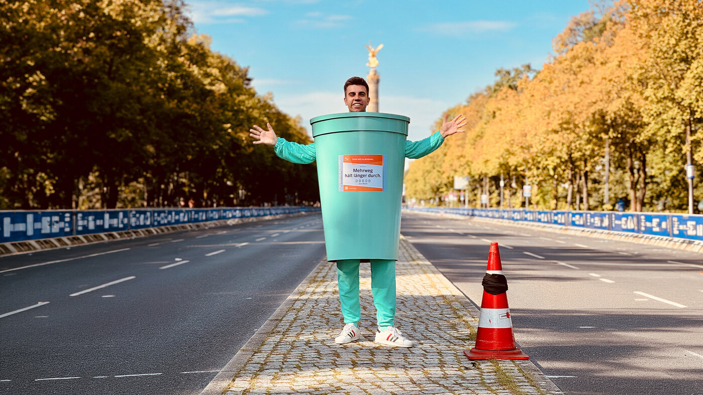 Person in einem übergroßen Mehrwegbecher-Kostüm auf der Berliner Marathonstrecke