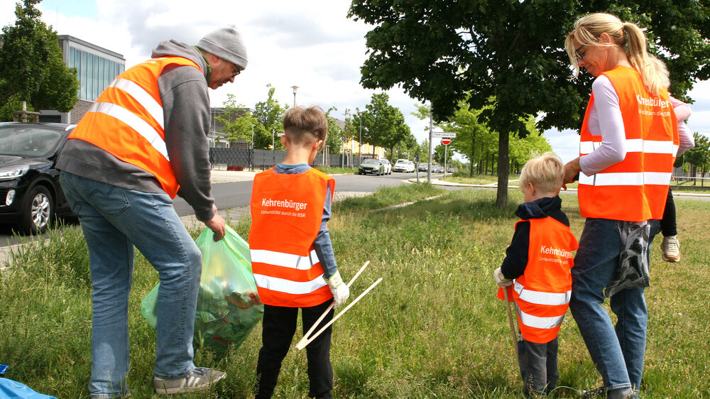 Freiwillige mit Warnwesten sammeln bei einer Kehrenbürger-Aktion Müll auf einer Grünfläche