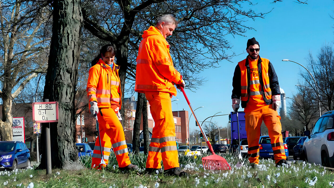 BSR-Mitarbeitende sammeln im Frühjahr Abfälle auf einer Grünfläche am Straßenrand ein