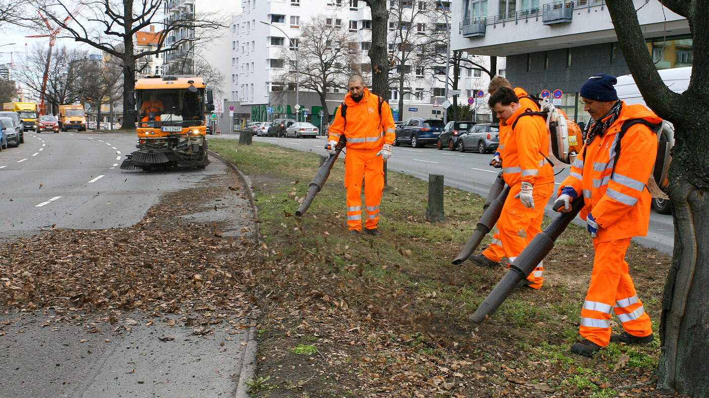 BSR-Mitarbeitende entfernen Laub am Straßenrand mit Laubbläsern und Reinigungsfahrzeug