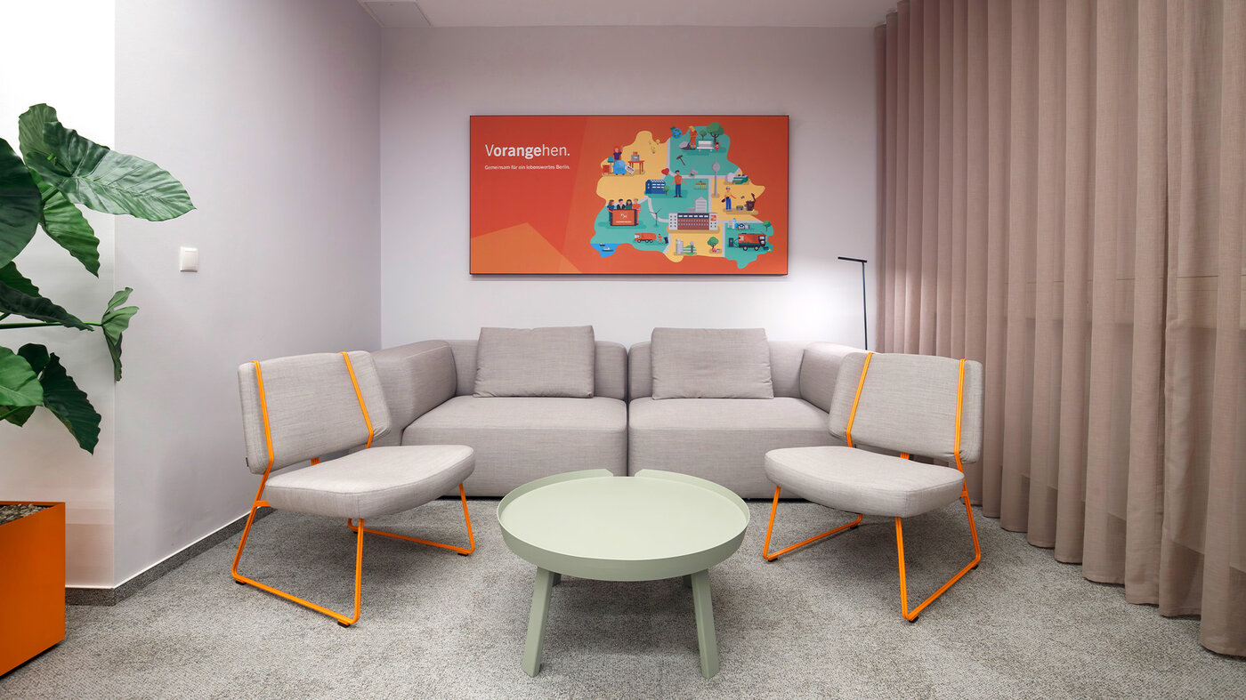 Gemütliche Sitzecke mit Sofa, Sesseln, rundem Tisch und dezenten Orangeakzenten